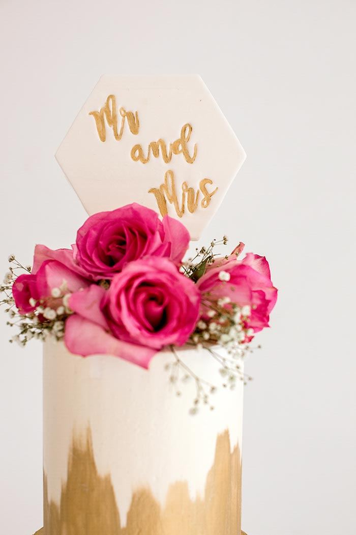 Wedding cake with magenta roses and gold drip under a Mr and Mrs topper