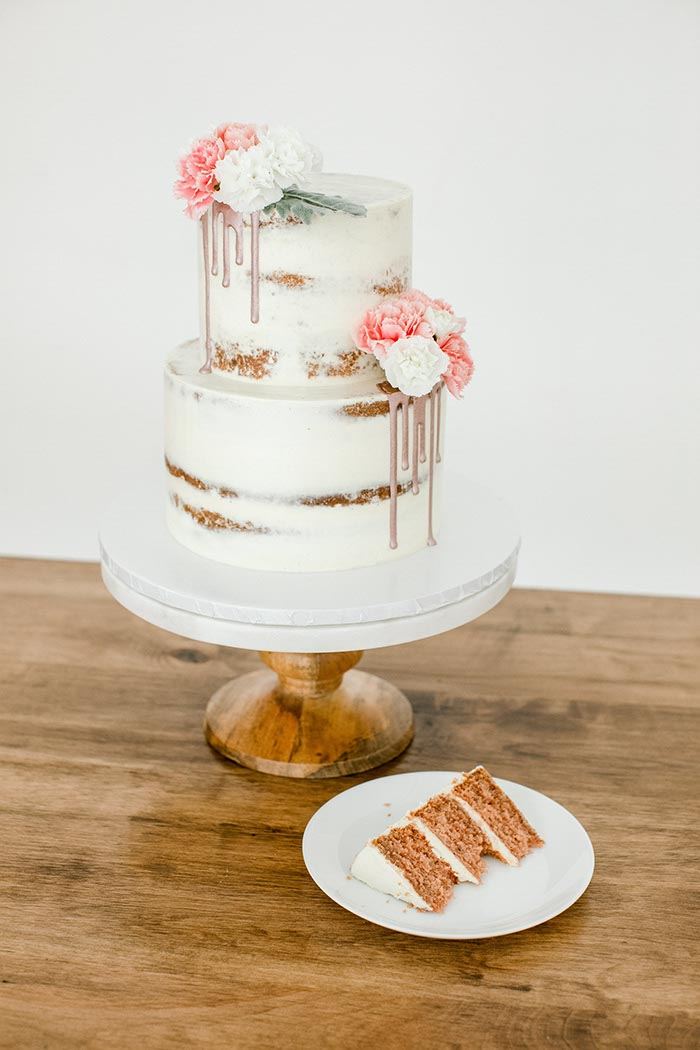 Semi-naked two-tier wedding cake with fresh flowers and a plated slice