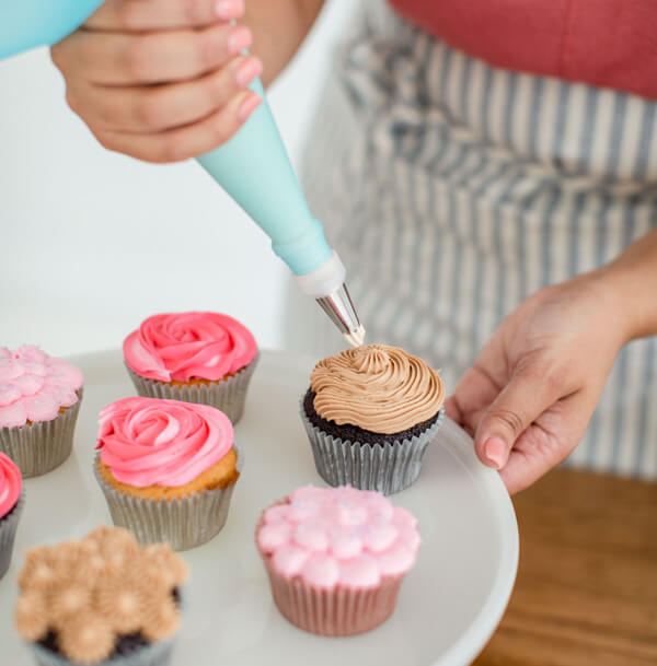 Hands piping rosettes onto cupcakes