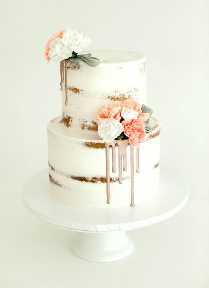Two-tier semi-naked wedding cake with a rose-gold drip and fresh flowers